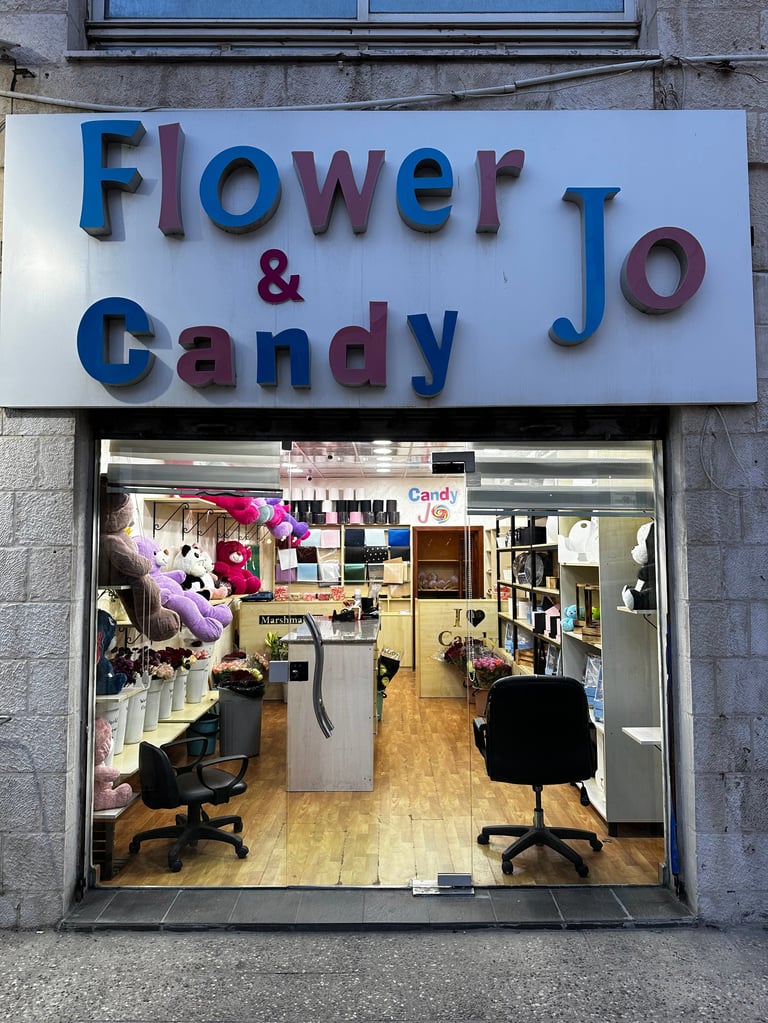 Storefront with blue and purple signage reading Flower & Candy Jo, displaying flowers and merchandise inside